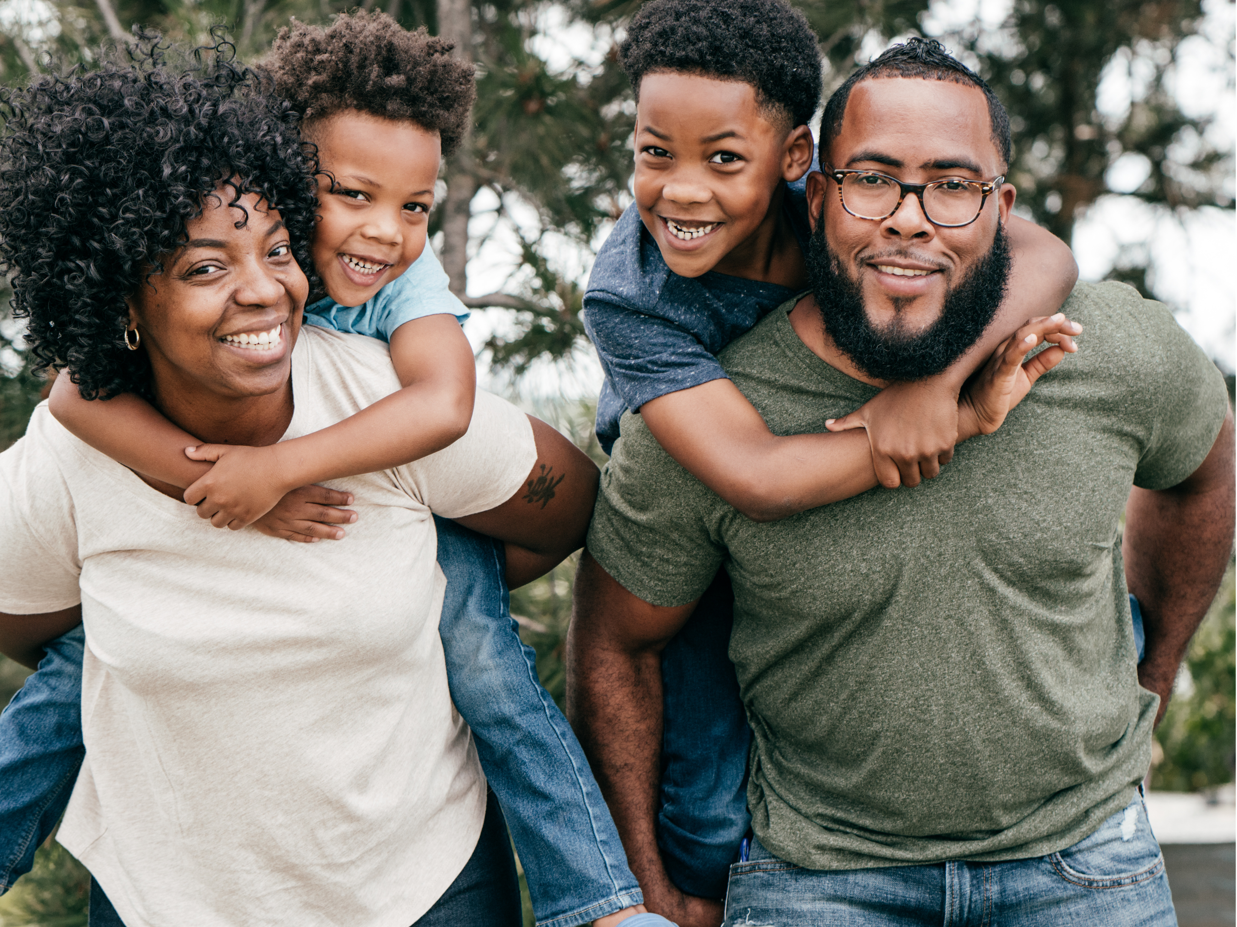 Parents smiling with their two young sons on their backs.