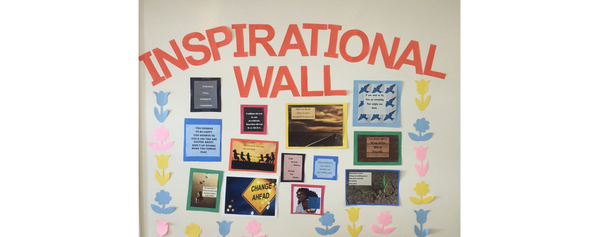 Bulletin board with "Inspiration Wall" and images and writings with paper flowers surrounding the items.