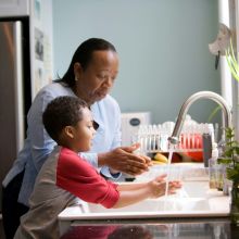 A woman and her child wash their hands at the kitchen sink.